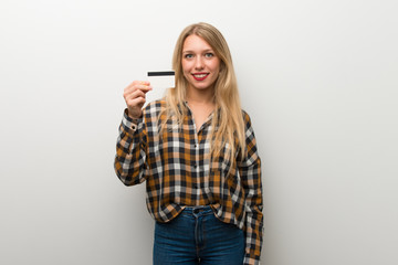 Fototapeta premium Blonde young girl over white wall holding a credit card