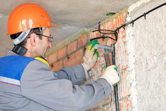 Electrician man construction worker installing fuse box electrical cable at house wall
