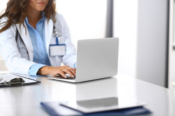 Unknown doctor woman typing on laptop computer while sitting at the desk in hospital office. close-up of hands. Physician at work. Medicine and health care concept