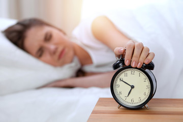 Alarm clock opposite of sleepy young woman stretching hand to ringing alarm willing turn it off....