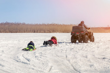 Man on ATV quadbike riding sledges with kids in tow on frozen lake surface at winter. Winter...