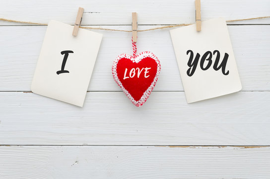 Paper stickers attached with clothespins on a rope and felt heart makes words I Love You on white wood planks background. Flat lay conceps Valentines day. Copy space. Trendy photo