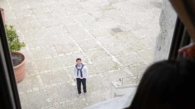 giovane donna osserva dalla finestre il suo uomo che esce dal cortile di casa 