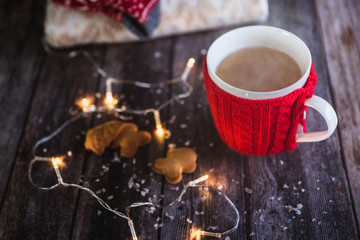 Woman hands holding Christmas coffee or tea red mug with steam, homemade gingerbread christmas cookies on a wooden table, sweeters on background