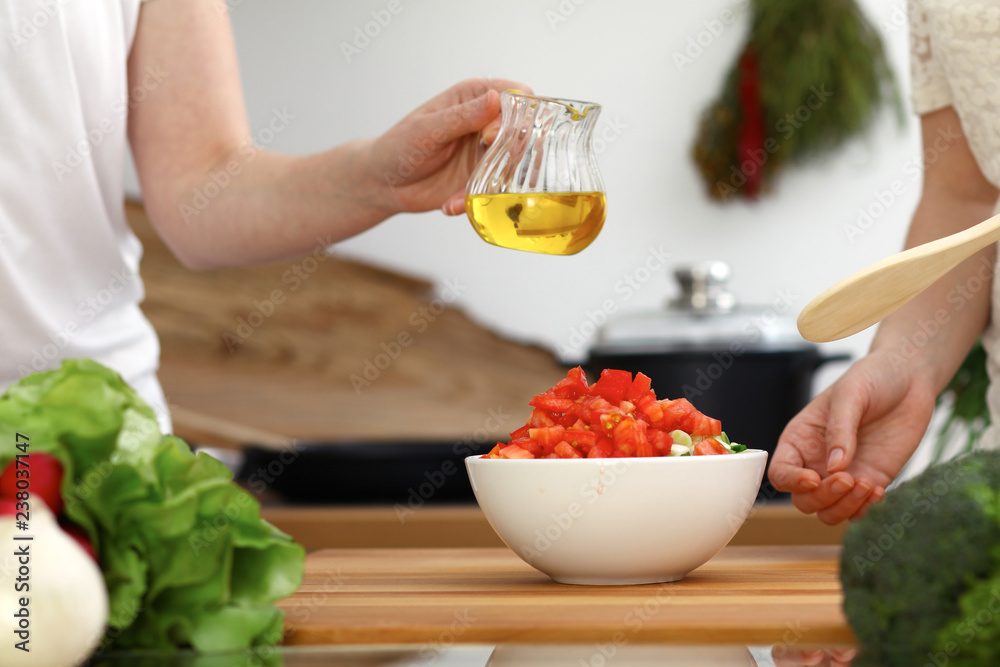 Wall mural Closeup of human hands cooking in kitchen. Mother and daughter or two female friends cutting vegetables for fresh salad. Friendship, family dinner and lifestyle concepts