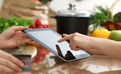 Close-up of human hands using tablet or touch pad. Two women in kitchen. Cooking, friendship or online shopping concepts