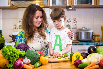 The young cook mother standing with her little son in the kitchen and salting vegetables