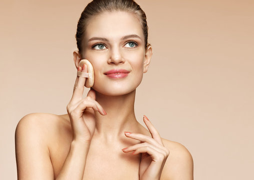 Woman applying dry powder using cosmetic cushion on her facial skin. Photo of attractive girl with perfect makeup on beige background. Beauty concept