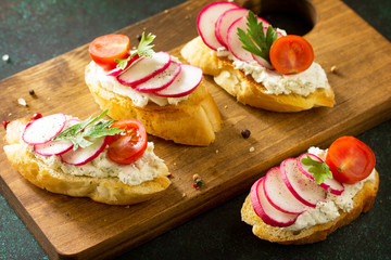 Antipasti snacks set for Wine. Brushetta or Crostini with Toasted Baguette,  Cheese, Radish and Tomatoes served on a rustic wooden board on a stone table.
