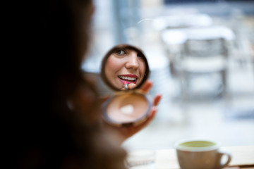 Beautiful young woman reflection making make-up near mirror ain the coffe shop.