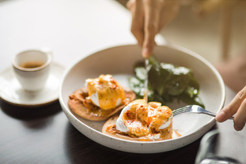Lunch Time at Cafe. Person eating sandwich with poached egg for lunch drinking espresso table close-up