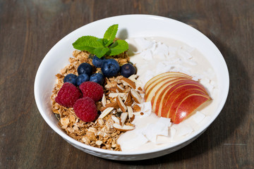 oat granola with apples and berries on wooden background, closeup