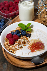 oat granola with apples and berries on wooden background, vertical closeup