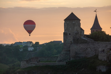 Fototapeta na wymiar Air balloon flies close to walls of medieval Castle Kamianets-Podilskyi