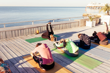 Group of young sporty women practicing yoga under instructors guidance working out outdoors by the...