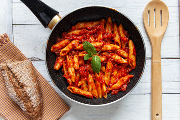 Sarten with bolognese macaroni, mint leaves and wooden spoon seen from above