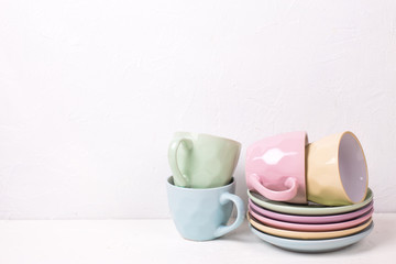 Pile of colourful tea cups and saucers on white textured background.