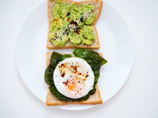 Appetizing bruschetta with egg and avocado on a plate. On the Sandwich, the avocado pulp and fried quail egg. Dark background. View from above. Close-up. Macro photography.