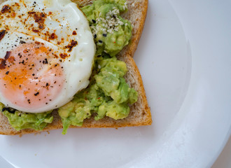 Appetizing bruschetta with egg and avocado on a plate. On the Sandwich, the avocado pulp and fried quail egg. Dark background. View from above. Close-up. Macro photography.