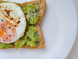 Appetizing bruschetta with egg and avocado on a plate. On the Sandwich, the avocado pulp and fried quail egg. Dark background. View from above. Close-up. Macro photography.