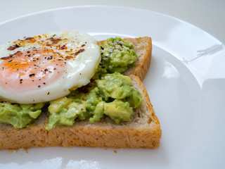 Appetizing bruschetta with egg and avocado on a plate. On the Sandwich, the avocado pulp and fried quail egg. Dark background. View from above. Close-up. Macro photography.