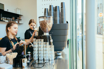 Friendly young female barista in apron with two braids preparing coffee working order. Small...