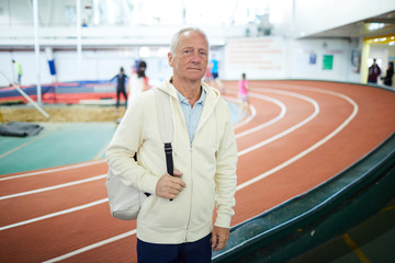 Active senior man in white hoodie carrying backpack on shoulder while visiting stadium