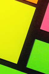 Green, yellow, orange and rose hue colorful office stickers on black paper. Office noteparer as...
