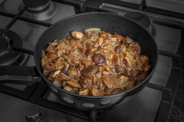 Fried Imleria badia mushrooms in a frying pan. Cooked boletus badius with onion on griddle.