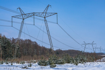 High-voltage power lines in winter time at snowy forest. High voltage electric transmission tower...