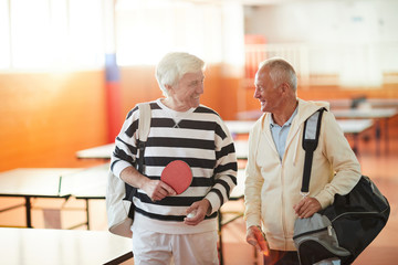 Active senior men with sportsbags and rackets going to play ping pong in the hall at leisure