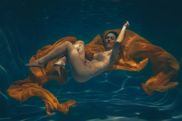 cute sporty girl swims underwater as a free diver in sheer jumpsuit alone