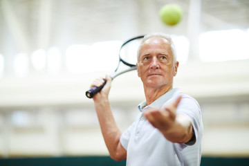 Mature professional player throwing tennis ball and looking at it before hitting with racket