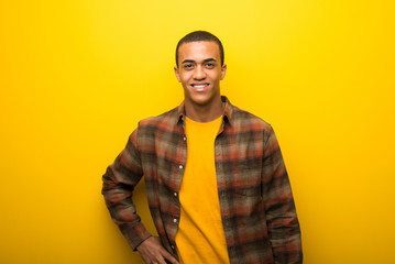 Obraz premium Young african american man on vibrant yellow background posing with arms at hip and smiling