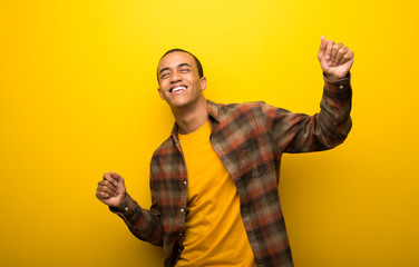 Young african american man on vibrant yellow background enjoy dancing while listening to music at a party