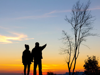 Fototapeta na wymiar Silhouette of happy couple standing on the mountain at the sunset or sunrise time.