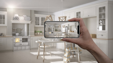 Hand holding smart phone, AR application, simulate furniture and interior design products in real home, architect designer concept, blur background, scandinavian white kitchen
