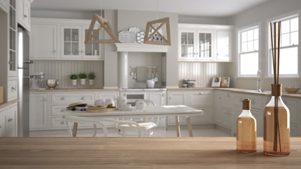 Wooden table top or shelf with aromatic sticks bottles over blurred scandinavian classic kitchen with dining table and chairs, morning light, white architecture interior design