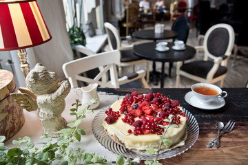 Vintage cafe, on the old steel cake with berries, a cup of tea, a milk jug and a bear with wings