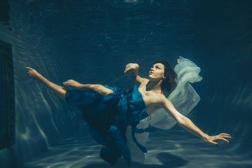 elegant pretty woman swims underwater like a free diver in a blue evening dress alone