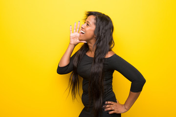 Young afro american woman on vibrant yellow background shouting with mouth wide open to the lateral