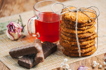 Oatmeal cookies with red tea and chocolate bars on wooden background. Still life in a rustic style.