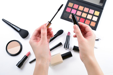 Mascara in woman hands. Professional makeup products with cosmetic beauty products, foundation, lipstick,  eye shadows, eye lashes, brushes and tools.