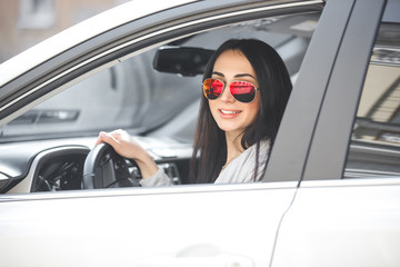 Young attractive woman in the car. Woman drive an auto. Close up portrait of beautiful woman outdoors. Urban lady.