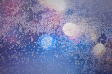 Fototapeta premium Winter background in soft pastel colors. Frost and snowflakes on the window. Multicolored bokeh with blur. Glare through glass. Background for holiday greetings with winter theme.