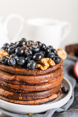 Stack of homemade chocolate pancakes with blueberries and chocolate pieces, light grey background