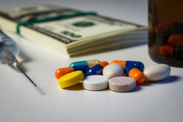 Blue-orange capsules, syringe and pills on the table with a pack of dollars