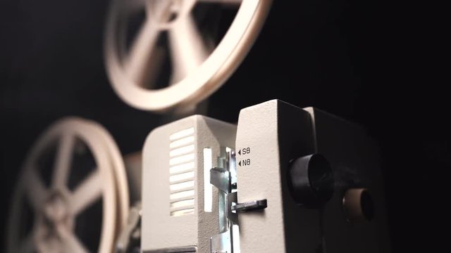 Vintage objects, cinematograph concept. Retro film projector playing in the dark room. Old-fashioned antique super 8mm film projector projecting beam of light.