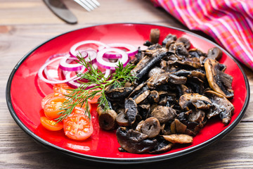 Fried mushrooms, onion and cherry tomatoes on a plate on a wooden table
