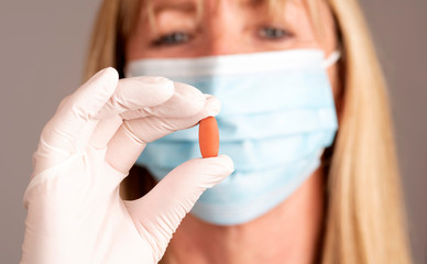 Woman wearing a mask holding a prescription tablet in a gloved hand